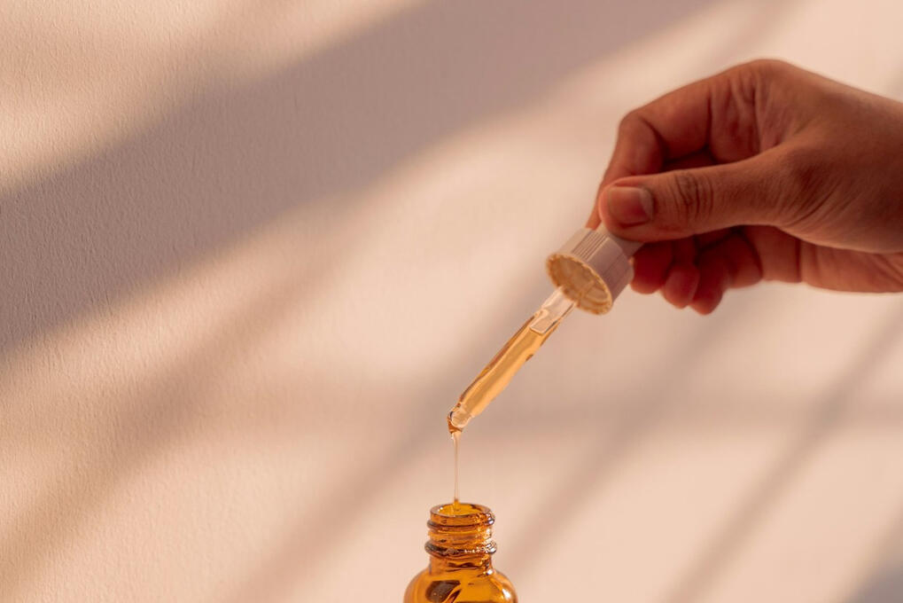 Dropper releasing a drop of golden serum into an amber glass bottle