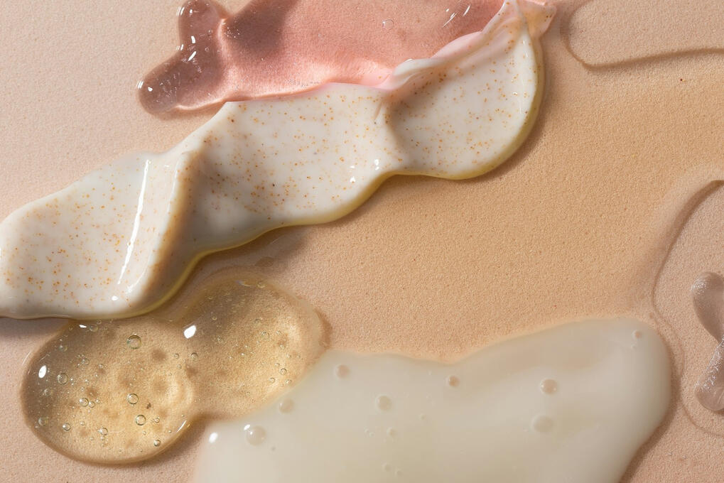 Swirls of pink gel, textured cream and clear serum on a beige surface
